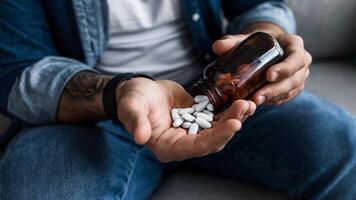 Man pouring capsules from bottle, hold pills on hand. Overdose of medication and pain. Depressed sad unhappy millennial caucasian guy wants to die, commit suicide, cropped, close up, , empty space photo