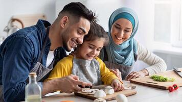 Cheerful middle eastern family of three making healthy dinner together in kitchen, happy islamic parents enjoying cooking with their little daughter, preparing tasty food at home, closeup photo
