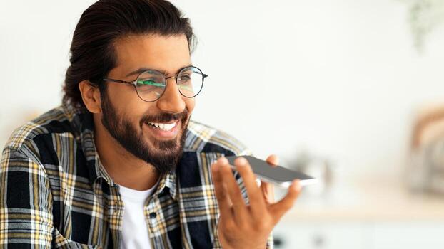 hermoso barbado árabe chico en lentes grabación audio mensaje en móvil teléfono, teniendo conversacion con su amigo o amante, de cerca retrato, Copiar espacio. moderno tecnologías y comunicación concepto foto