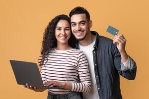 Online Shopping Concept. Happy Arabic Couple Using Credit Card And Laptop While Standing Over Yellow Background In Studio, Cheerful Middle Eastern Man And Woman Enjoying Purchasing In Internet photo