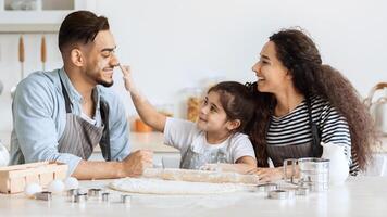 Happy middle-eastern family playing with flour while making dough for cookies, cheerful father, mother and cute little daughter spending time together, baking pastry at kitchen, panorama photo