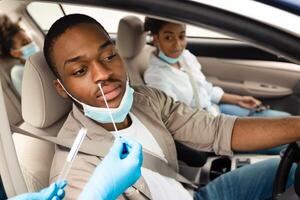 Black Family Getting Tested For Coronavirus Sitting In Car, Wearing Face Masks At Drive-Thru Covid-19 Testing Site. Coronavirus Diagnostic, Traveling And Tourism In Pandemic Concept photo
