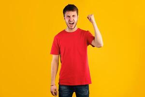 Hate, Rage And Anger. Portrait of young mad guy shaking clenched fist to camera, screaming and shouting, posing at studio, standing isolated over blue background wall. Angry man threatening photo