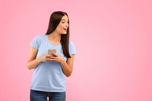 Portrait of smiling curious woman using smartphone standing isolated over yellow studio background, looking away, peeking and trying to see something, holding gadget, copy space. Lady chatting online photo
