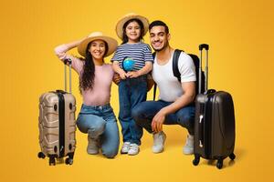 Ready For Vacation. Happy Arab Family Of Three With Suitcases Posing Together Over Yellow Background, Cute Little Middle Eastern Girl Holding Small Globe, Enjoying Travelling With Parents, Free Space photo