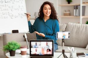 Modern Teacher. Smiling Woman Filming Virtual Lecture For Educational Blog Sitting In Front Of Laptop And Mobile Camera Indoors. Remote Tutoring And E-Teaching Concept. Live Streaming photo