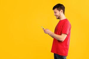 People, Technology And Communication Concept. Side view portrait of handsome man texting on his cell phone, isolated over blue studio background, copy space. Smiling guy chatting in social media photo