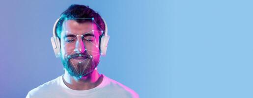 A man with headphones explores facial recognition technology while his face is analyzed through digital overlays. He appears relaxed, immersed in the experience against a gradient background. photo