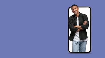 A person stands with their arms crossed and smiles while interacting with a large-screen smartphone. The background is a solid color, emphasizing the subject's engaging demeanor. photo