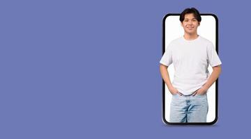 A young man stands confidently with his hands in pockets, positioned within a smartphone. He is ready to connect online using a social media application on the large screen. photo