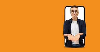A young man with glasses smiles widely while presenting with open hands, framed within a large smartphone screen. The vibrant background adds energy to the scene. photo