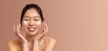 Asian woman smiles while applying skincare products on her face, embracing a pampering session. The soft, muted background enhances her relaxed and joyful atmosphere, inviting self-care. photo