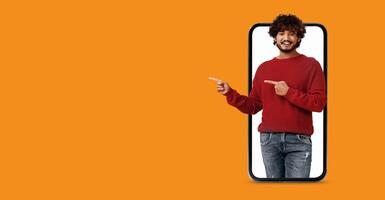 A person interacts with a large smartphone display, enthusiastically pointing to the screen. The bright orange background adds energy, highlighting modern technology and social media use. photo