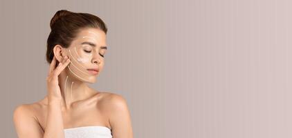A woman engages in her beauty routine, applying skin care products to her face. She is isolated against a soft, neutral background, creating a calm and relaxing atmosphere for self-pampering. photo