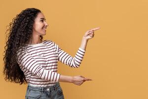 Great Promo. Happy Arab Couple Pointing At Copy Space In The Middle With Two Hands, Cheerful Young Spouses Demonstrating Empty Place On Yellow Background For Your Advertisement, Panorama photo
