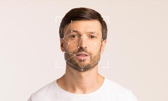 A man stands against a light backdrop, displaying facial recognition technology. Geometric patterns overlay his face, illustrating advancements in identification and biometric analysis. photo