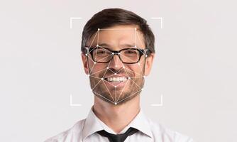 A man with glasses smiles as facial recognition technology highlights his features. The setting is minimalistic with empty space, emphasizing the focus on face identification. photo