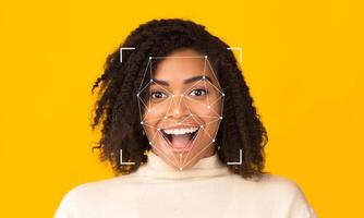 A woman with curly hair expresses excitement while facial recognition technology scans her features. The bright yellow background enhances the focus on her expression and the technology at work. photo
