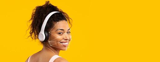 A woman is wearing headphones and smiling while showing facial recognition patterns on her face against a bright yellow background. This highlights innovative identification technology. photo