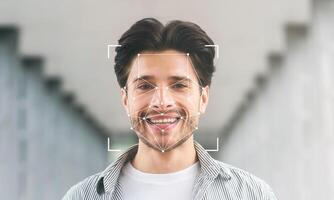 A smiling young man stands in a modern corridor, surrounded by soft lighting. His face is framed by digital facial recognition technology, highlighting identification features. photo