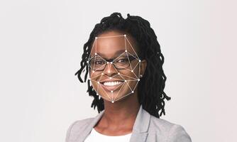 A smiling woman with glasses and dreadlocks is showcased against a light background, highlighting facial recognition technology. The focus is on her joyful expression and the technology overlay. photo