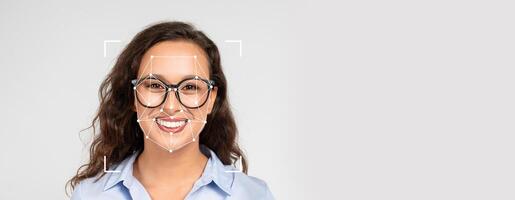 A smiling woman with glasses displays her face, showcasing the application of facial recognition technology for identification purposes in a blank setting. The focus is on her expressive features. photo