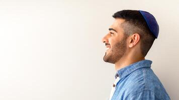 Happy Person. Profile side view portrait of handsome cheerful jewish guy posing at studio, smiling and looking aside, wearing kipa, posing isolated on light background copy free space, advert banner photo