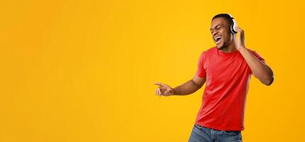 Funny African Man Singing And Dancing Having Fun Posing Wearing Wireless Earphones In Studio Over Yellow Background. New Musical Application Advertisement. Black Guy Enjoying Great Playlist photo