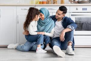Happy Islamic Parents Bonding With Their Little Daughter In Kitchen, Portrait Of Cheerful Smiling Middle Easter Family Of Three Relaxing On Floor, Enjoying Spending Time Together, Free Space photo