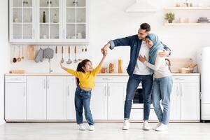 Portrait Of Happy Muslim Family Of Three Having Fun At Home Together, Islamic Mother In Hijab, Father And Their Little Daughter Dancing In Kitchen, Parents Looking At Their Adorable Child photo