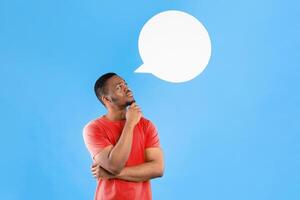 My Thoughts. Thoughtful African American Man Posing With Empty Speech Bubble Above Head Standing On Blue Studio Background. Let Me Think Concept. Vertical Shot photo
