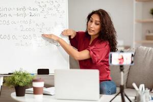 Remote Lecture. Young lady teacher explaining math formulas, giving online lesson, sitting at desk, filming vlog. Lady recording blog for her internet channel and making live videochat photo