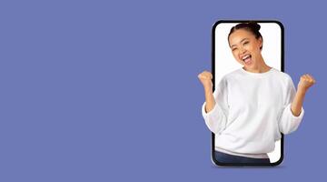 A young individual expresses joy and triumph while interacting with a smartphone. The person is in an isolated environment, highlighting the connection of technology and emotions. photo