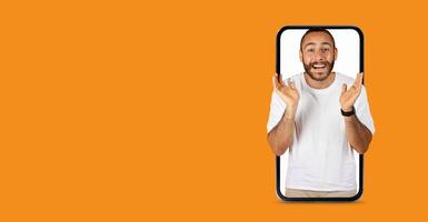 A person with a big smile is appearing to engage in lively communication through a large smartphone screen. The lively expression conveys excitement, enhancing the vibrant orange background. photo