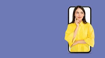 A young woman in a yellow top appears to be deep in thought as she interacts with a smartphone featuring a large screen. The background is a solid color, providing a modern feel. photo