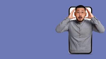 A person appears to be shocked or surprised, holding their head inside a large smartphone frame. This moment captures the impact of technology on communication and social interaction. photo