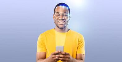 A young man with a cheerful expression uses his smartphone to engage in face recognition technology. The background is a simple gradient, emphasizing the modern tech experience. photo