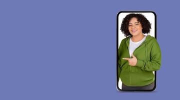 A cheerful individual gestures towards a large smartphone screen, showcasing the use of social media. The setting is simple and focused, emphasizing connection through technology. photo