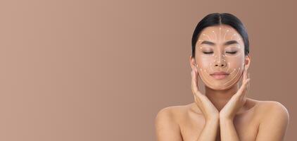 Asian woman is enjoying her skin care routine, applying techniques with her hands gently on her face. She is in a tranquil environment with a neutral background, emphasizing relaxation and pampering. photo