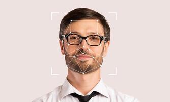 A man with glasses is standing against a neutral background while facial recognition technology highlights his features. This showcases advancements in ID technology and its applications. photo