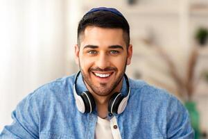 Online Call. Portrait of smiling jewish man in kipa having virtual conference with colleagues or students using computer, talkng and gestirung, sitting at desk at home office, webcamera view photo