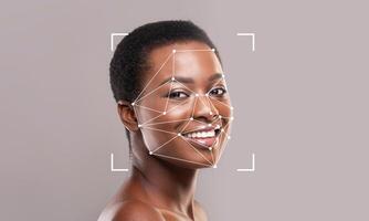 A woman with a bright smile poses in front of a gray background. Facial recognition technology overlays geometric lines and points on her face, illustrating identification capabilities. photo
