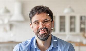 A smiling man is shown against a bright, modern kitchen background. Facial recognition technology highlights his features with geometric overlays, emphasizing identification capabilities. photo