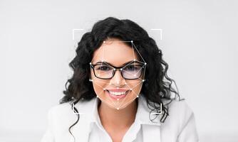 A woman smiling at the camera demonstrates facial recognition technology. Her facial features are being analyzed with an overlay marking key points for identification. The space around her is empty. photo
