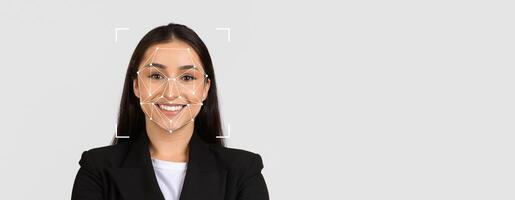 A woman with a confident smile stands against a gray background, demonstrating the application of facial recognition technology for identification. photo