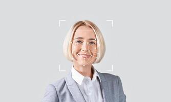 A professional woman smiles as facial recognition technology analyzes her features in a minimalistic setting. The soft background emphasizes the focus on identification processes. photo