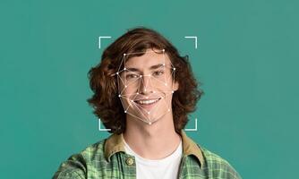 A young man with curly hair smiles confidently while facial recognition technology captures his features. The background is a solid color, highlighting the tech's application in identification. photo