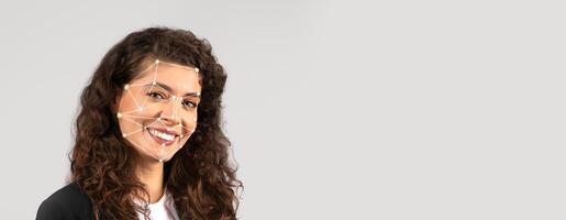 A woman with curly hair is smiling while facial recognition technology highlights key facial points on her face. The background is plain and empty, emphasizing her features. photo