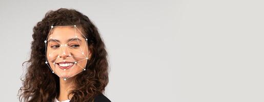 A woman with curly hair is smiling as facial recognition technology analyzes her facial features. The background is blank, emphasizing her expression and the technology in use. photo