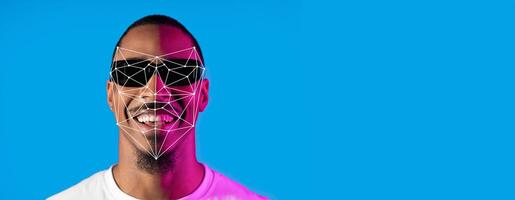 A person wearing sunglasses smiles confidently against a bright blue background. Facial recognition lines and points overlay the face, showcasing advanced identification technology in detail. photo